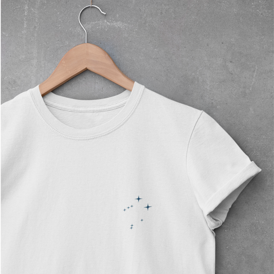 White Libra constellation t-shirt on a wooden hanger against a gray concrete wall.