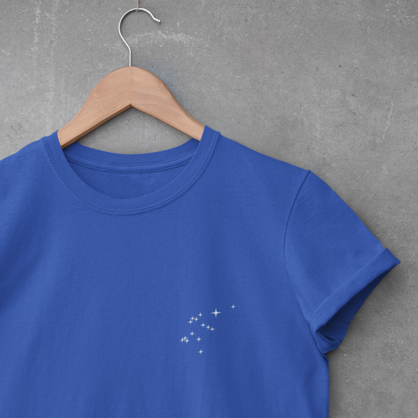 Royal Blue Aquarius constellation t-shirt on a wooden hanger against a gray concrete wall.