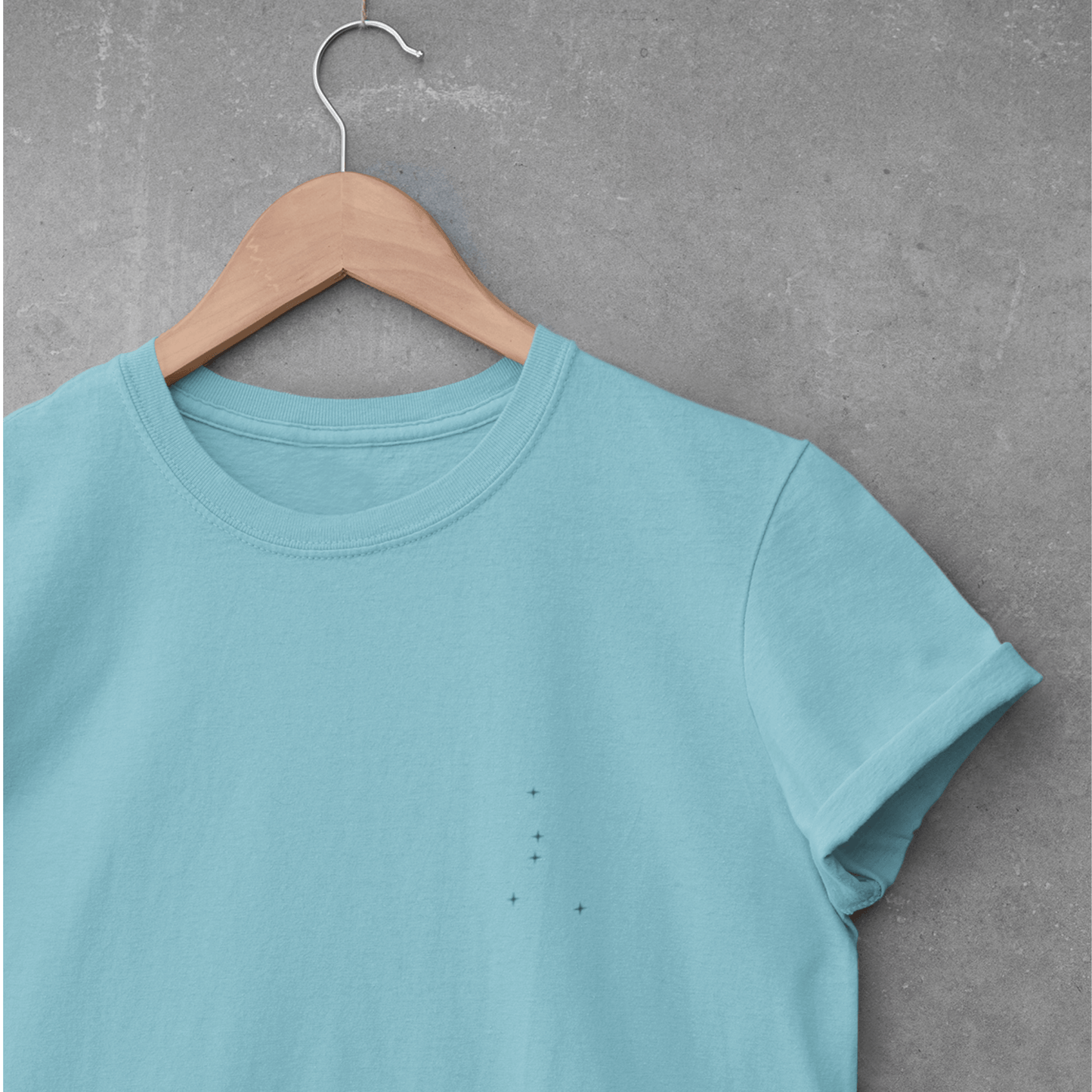 Turquoise Cancer constellation t-shirt on a wooden hanger against a gray concrete wall