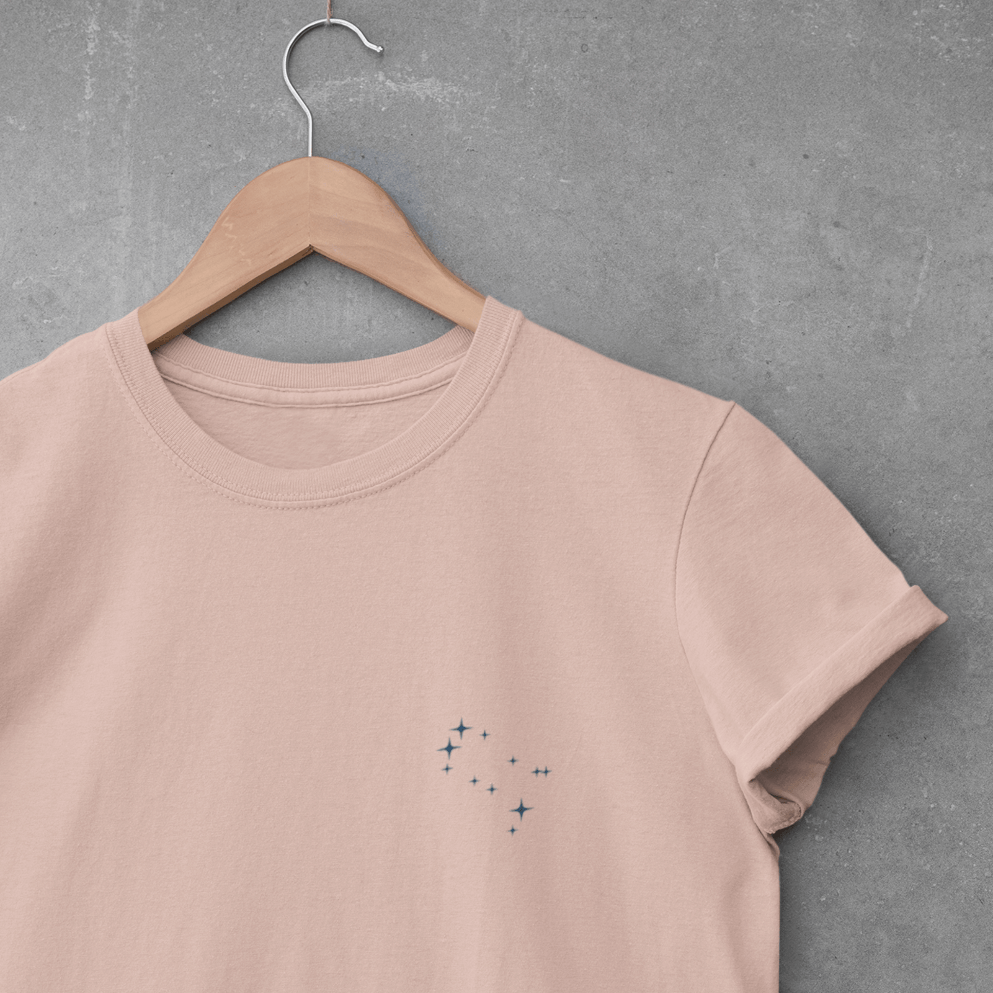 Gemini constellation t-shirt on a wooden hanger against a gray concrete wall.