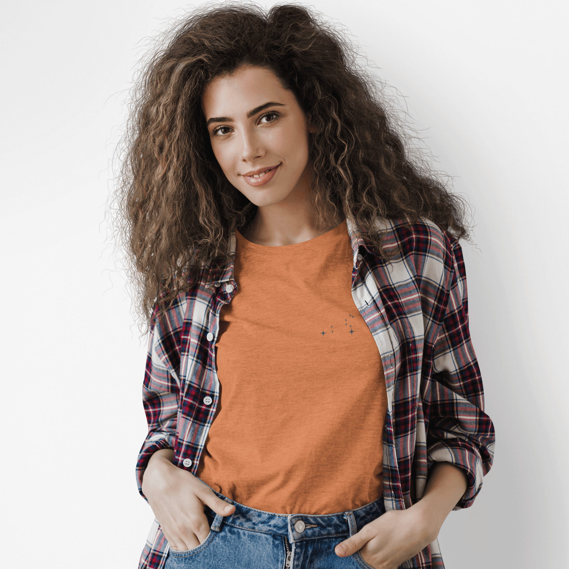 Woman wearing an orange Leo constellation tshirt and a flannel with a white background.