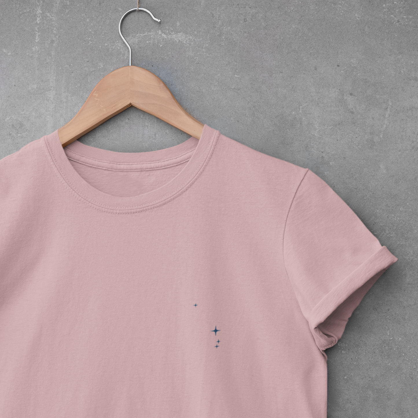 Orchid Aries constellation t-shirt on a wooden hanger against a gray concrete wall.