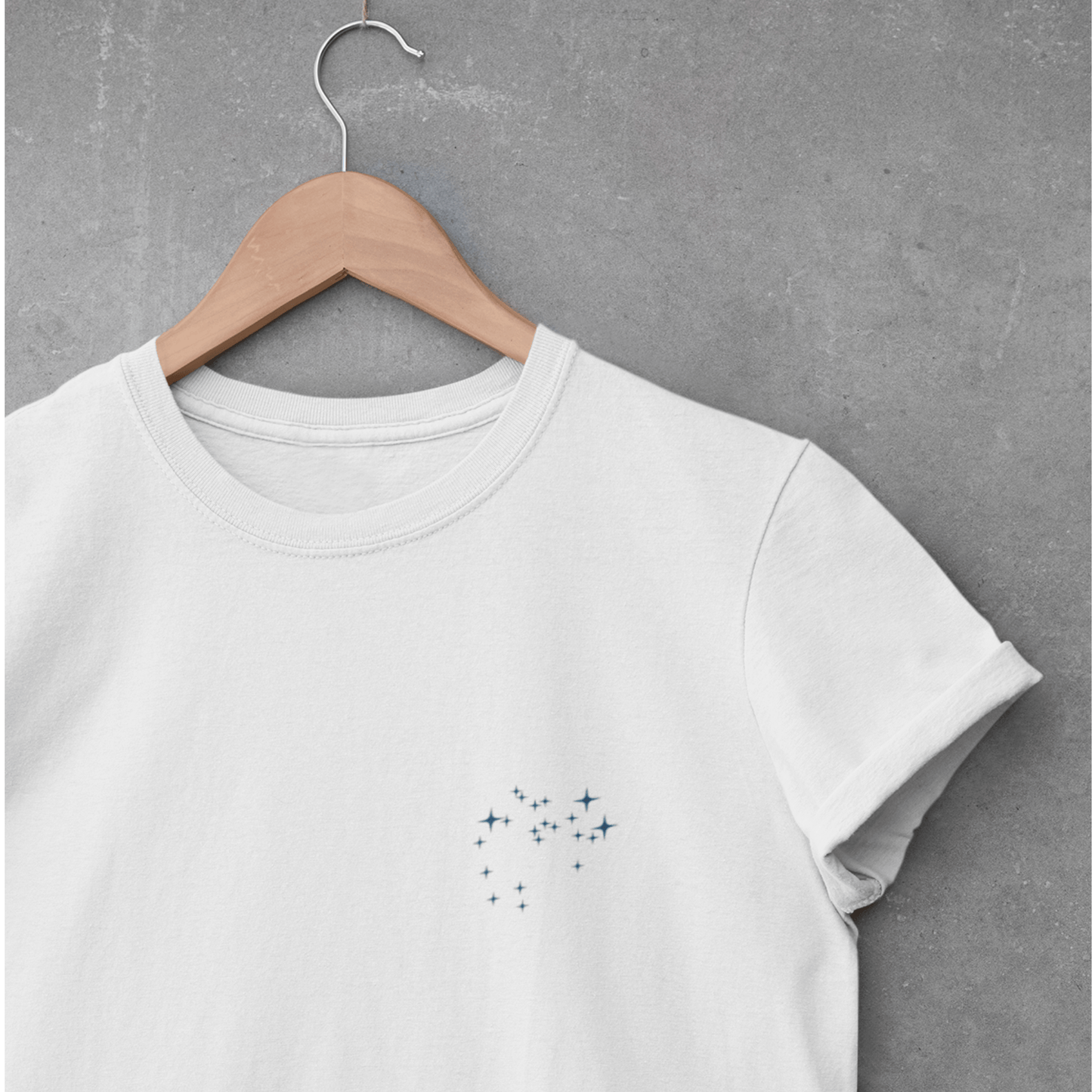 White t-shirt with a Sagittarius constellation on a wooden hanger against a gray concrete wall.