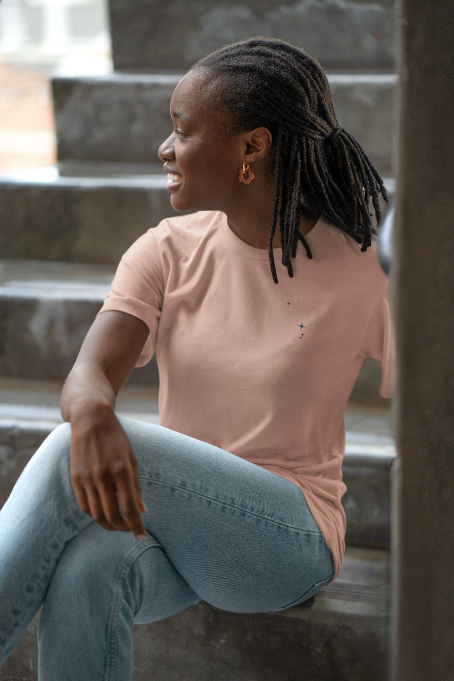 Woman sitting on steps wearing a peach Aries constellation t-shirt and light blue jeans.